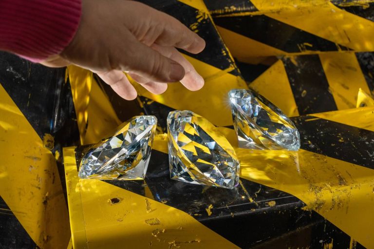 Hand, die nach gro&szlig;en Diamanten greift, die auf einem gelb-schwarzem Untergrund liegen